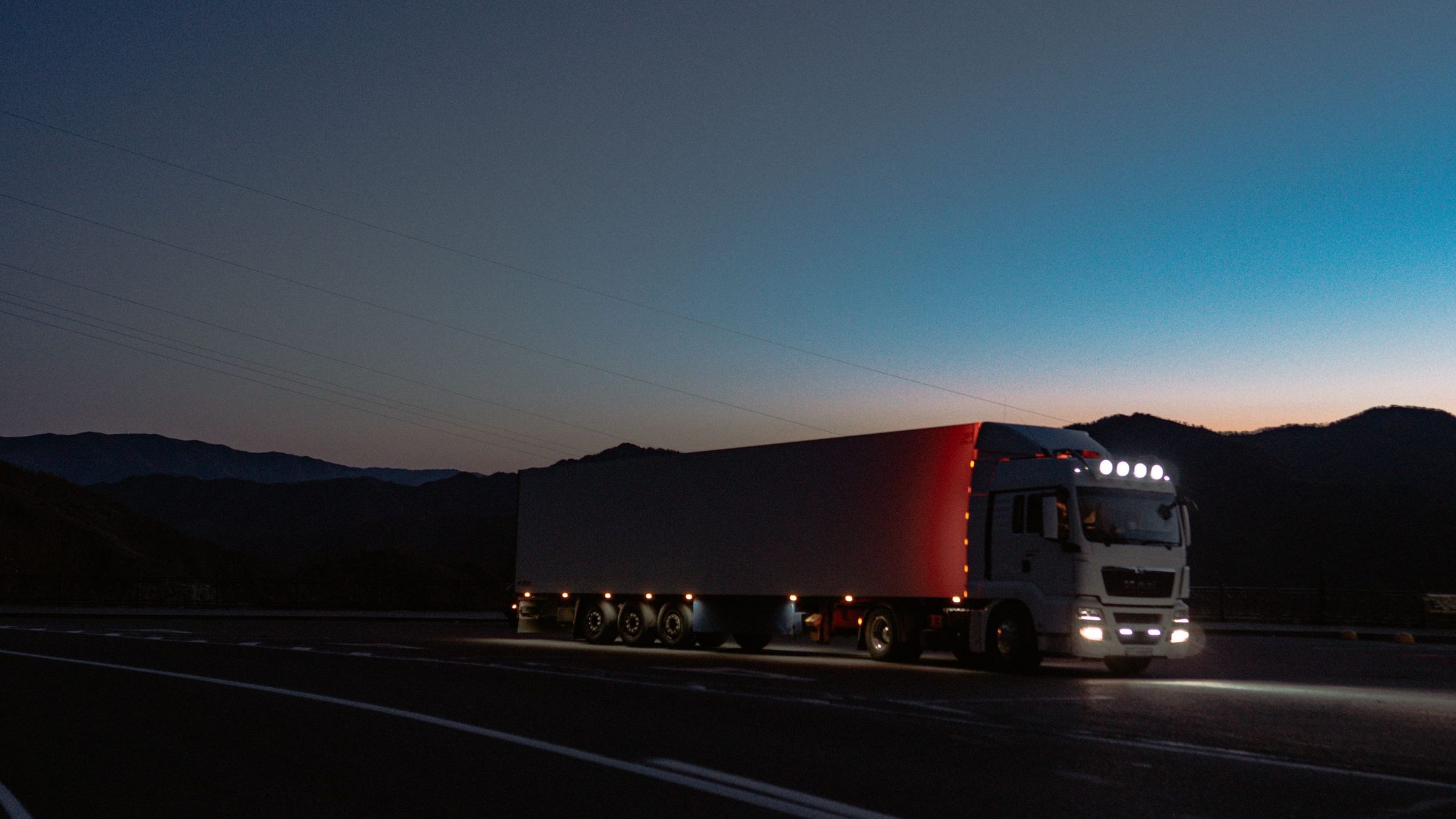 A truck on the road at dusk with its lights on